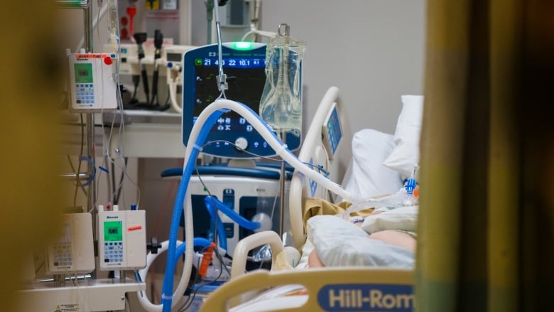 An unseen intubated person lies in bed in an ICU room.