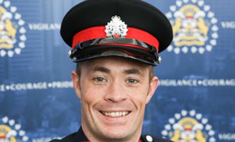 A Calgary police in his dress uniform poses in front of a wall of police logos.