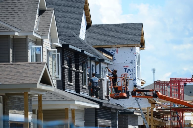 Construction workers put the finishing touches on houses being built in a new development of condos with peaked roofs.