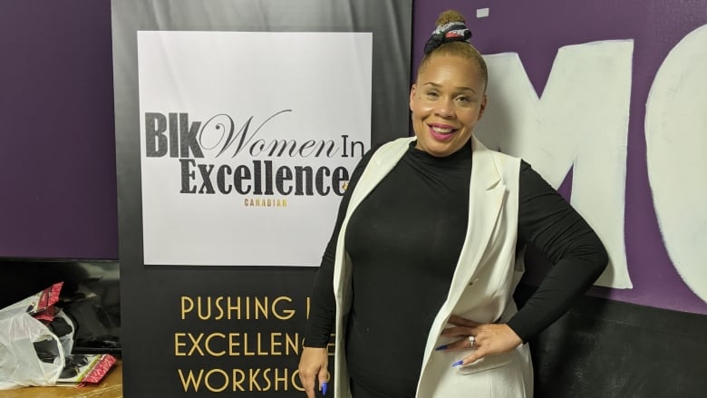 A Black woman standing beside a sign that reads 