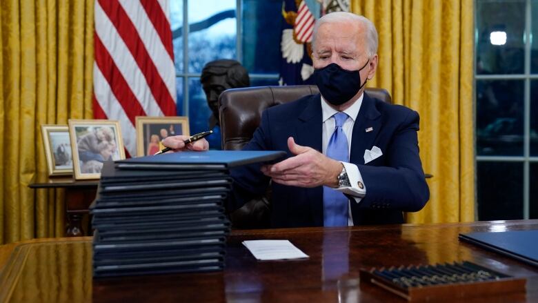 The President signs a stack of documents in black folders.