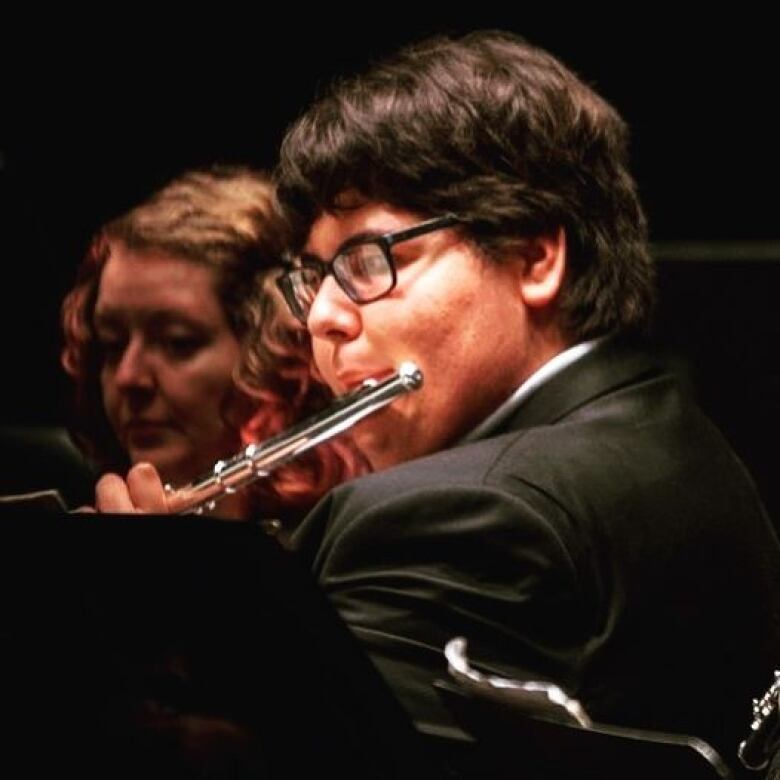 A young man playing a flute with an orchestra.