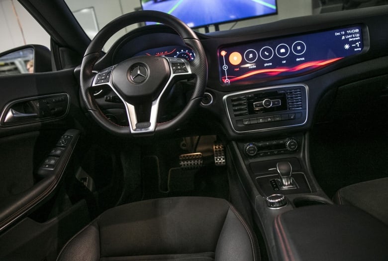 The inside of a Mercedes-Benz vehicle shows a steering wheel and large display screen.