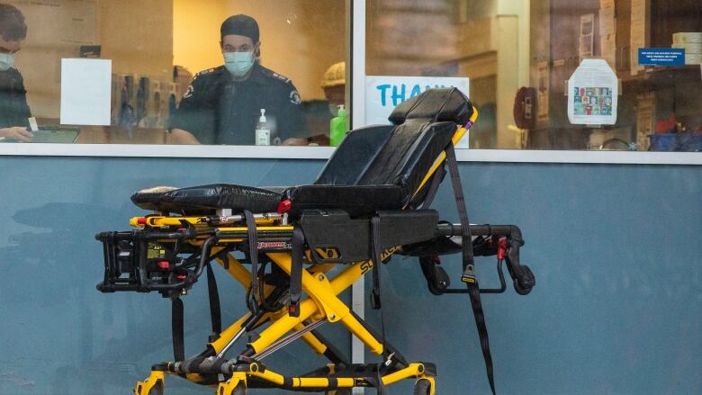 A man in black work attire is behind a window, with a stretcher in front of him.