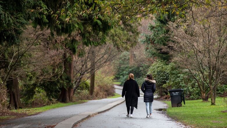 Two people with their backs to the camera walk along a forested path.