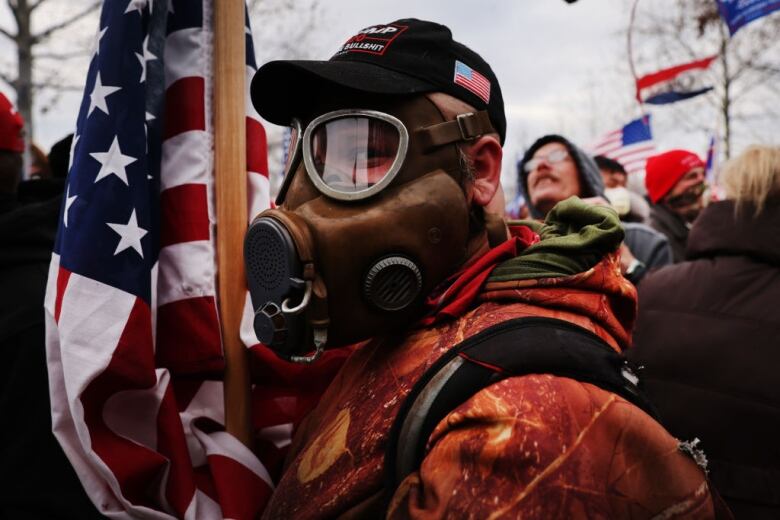 A Trump supporter holding an American flag is wearing a gas mask in a crowd of people storming the U.S. Capitol building on Jan. 6, 2021.