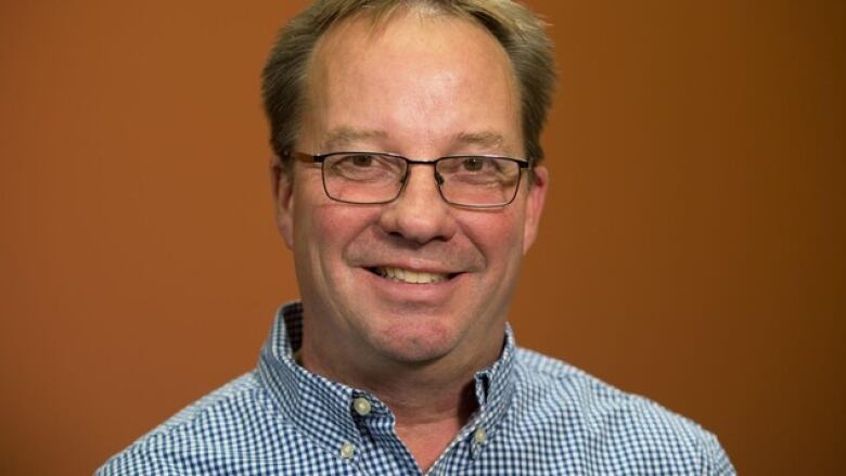 Close up photo of a smiling man in glasses in front of a plain background. 