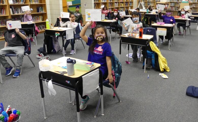 Young kids in a classroom hold up signs. 