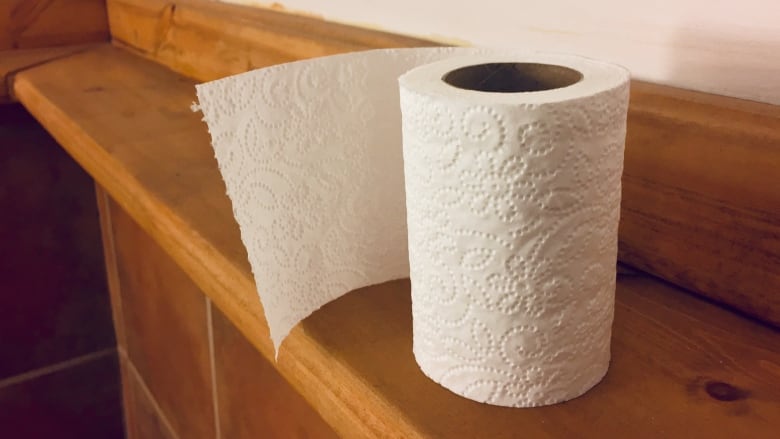 Partially used toilet paper roll standing up on wooden ledge