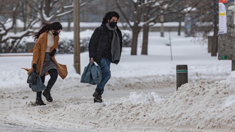 Two people walk up a hill in city after a snowstorm and before streets have been cleared.