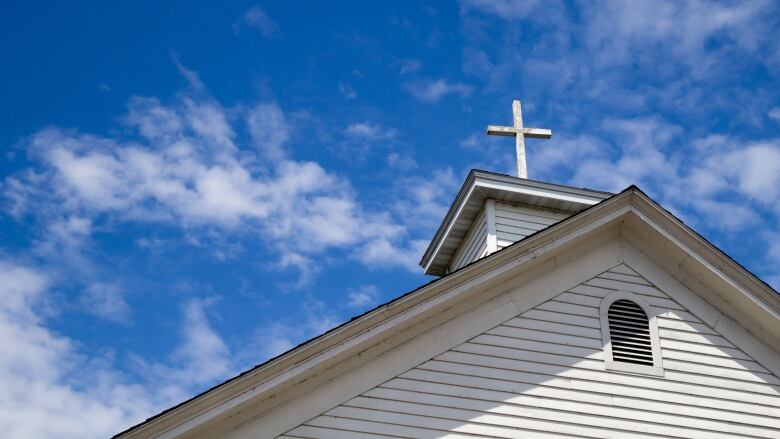 A cross is perched on the roof of a white church building. 