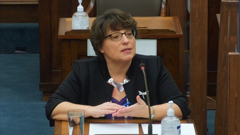 A woman with short brown hair and glasses sits inside the Prince Edward Island legislature. 