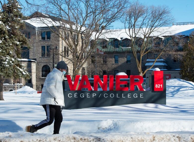 A person in a mask walks past a sign that says Vanier College.