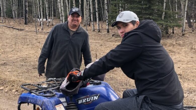 A man sits on a quad wearing a black hoodie and white ball cap.