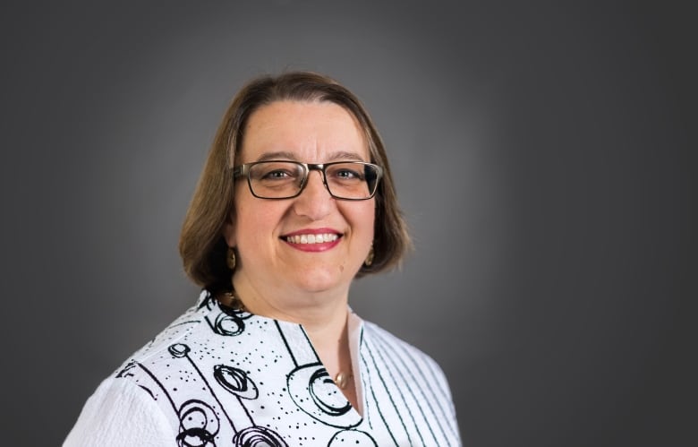 Woman wearing glasses and a white blouse with a black pattern.