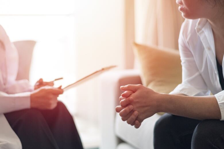 A stock photo shows two people talking. One person is holding a clipboard while the other has their hands clasped. 