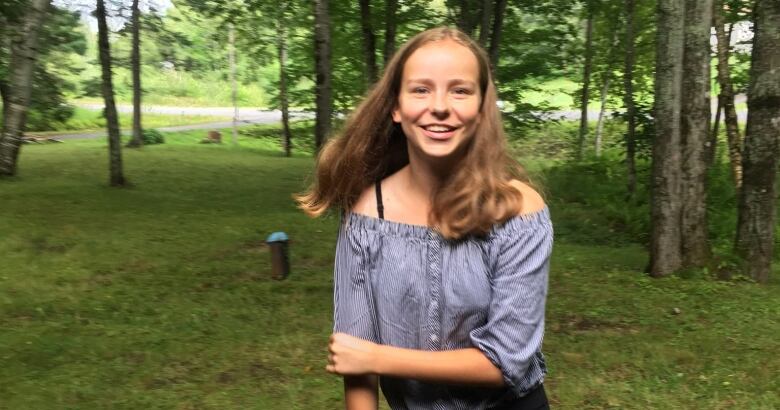 A portrait of a smiling teenage girl in a grassy area, surrounded by trees.