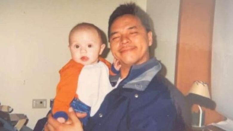 A man with a jacket, smiling and hold a baby. 