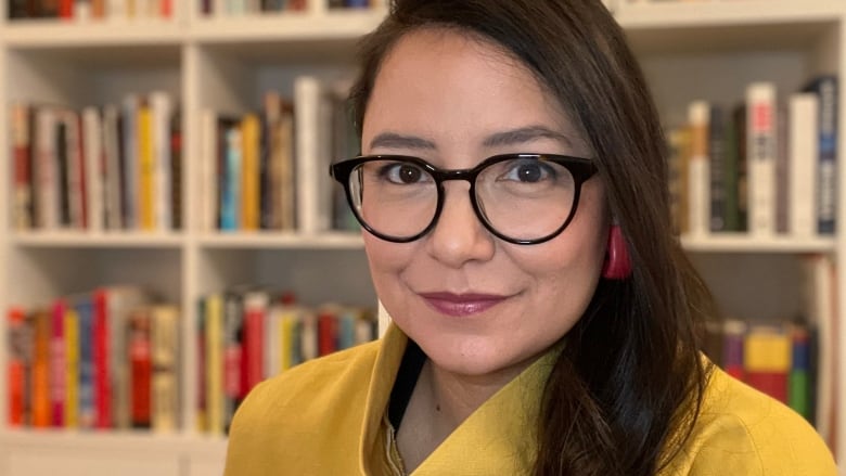 A woman with glasses poses for a photo in front of some well-stocked bookshelves.