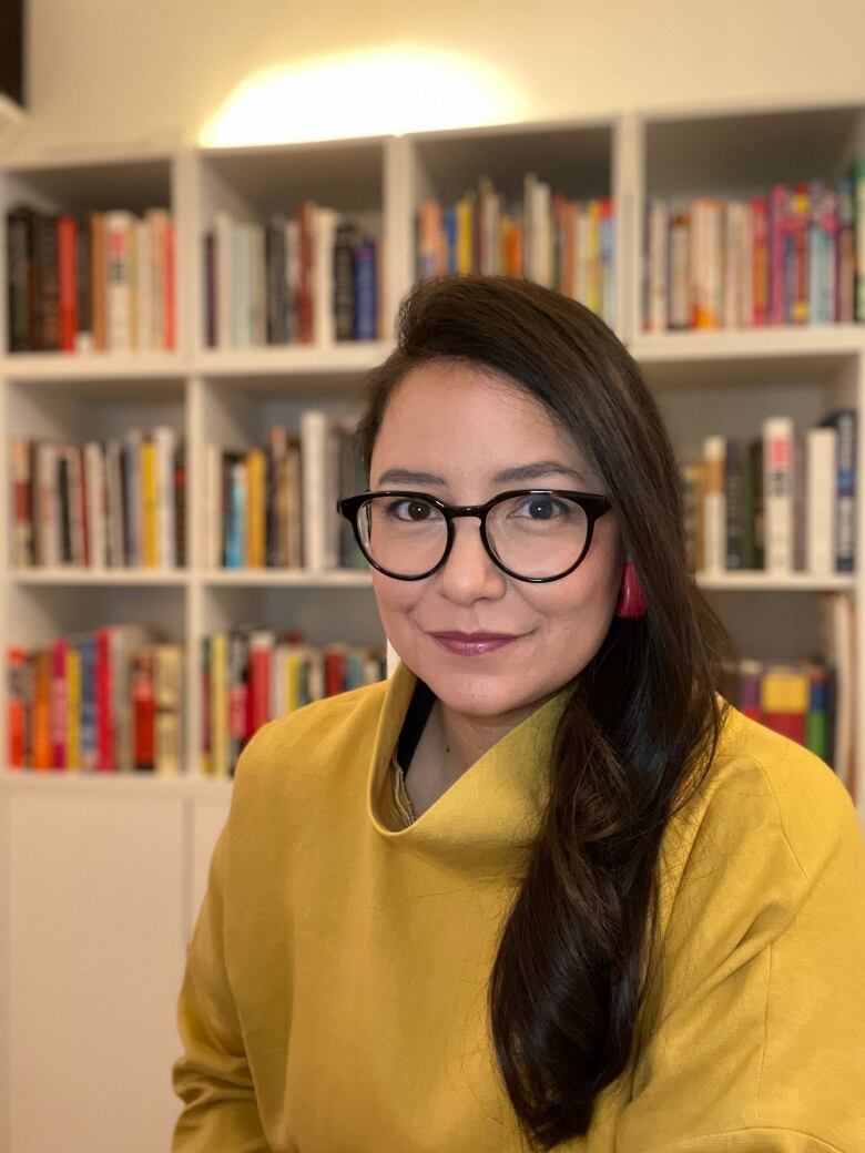 A woman with glasses poses for a photo in front of some well-stocked bookshelves.