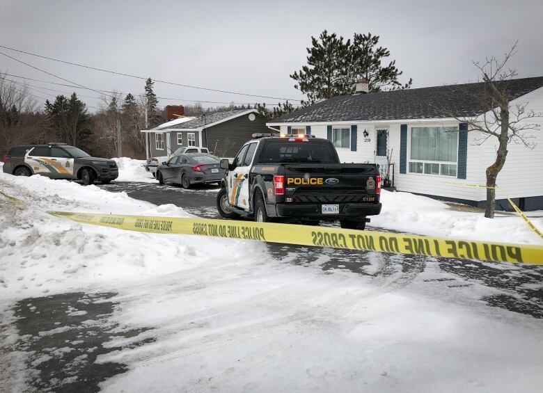 Yellow police tape blocks access to a home's driveway, which contains several police vehicles.