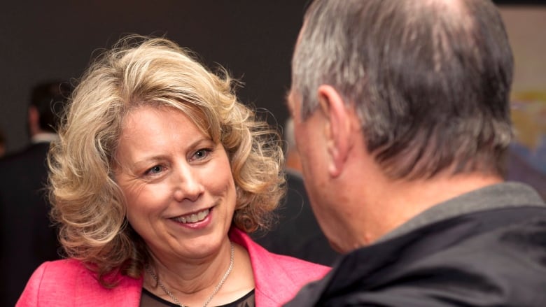 A woman wearing a pink blazer speaks to a man. 