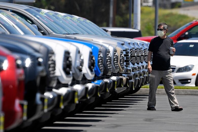 A man wearing a mask walks in front of a long row of trucks for sale.