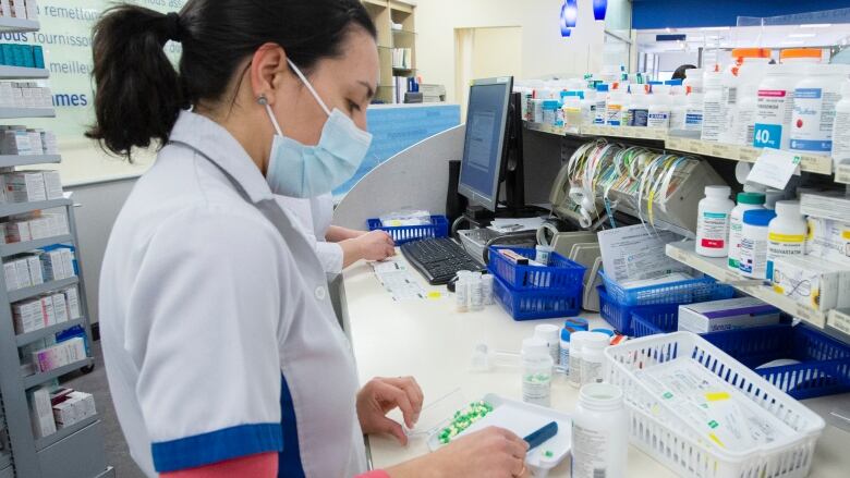 A pharmacist in a white jacket counts pills behind the counter.