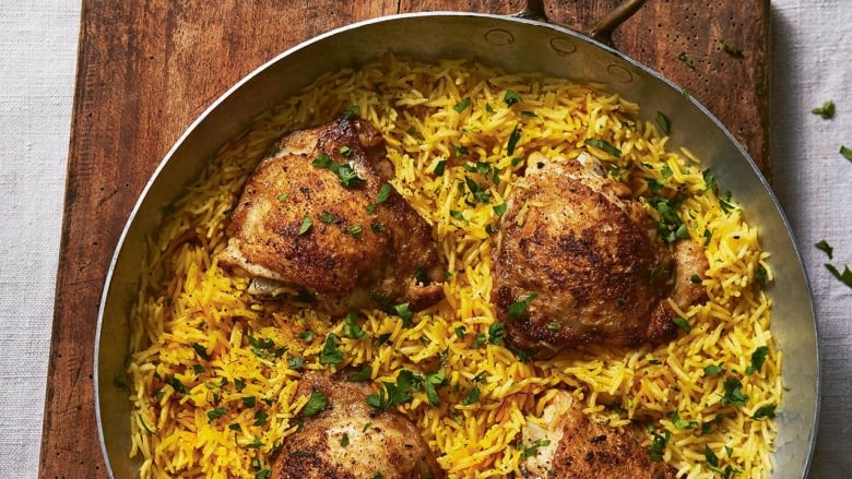 Overhead shot of a metal pan with cooked rice and chicken thighs. It's sitting on a wooden cutting board on a grey tablecloth. 