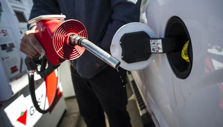 A man holds a leaking gas nozzle at a station while filling his car. 