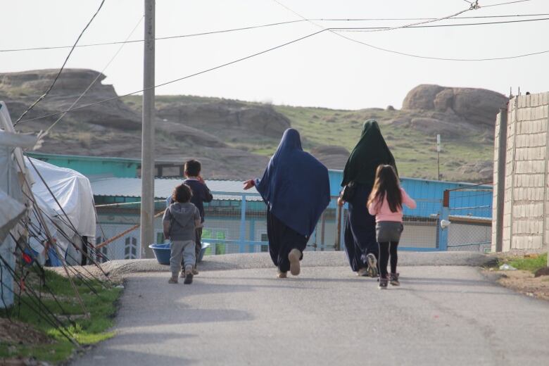 Women and children walk down a road in a detension camp in Syria.