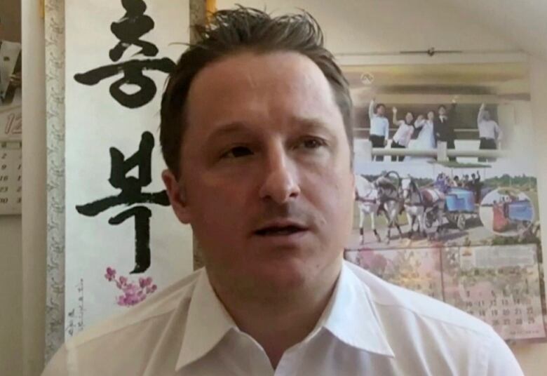 A man wearing a white collared shirt sits in front of a calendar.