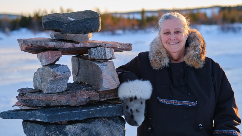 A woman smiles next to a pile of stones. There's snow all around her. 