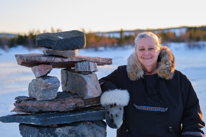 A woman smiles next to a pile of stones. There's snow all around her. 