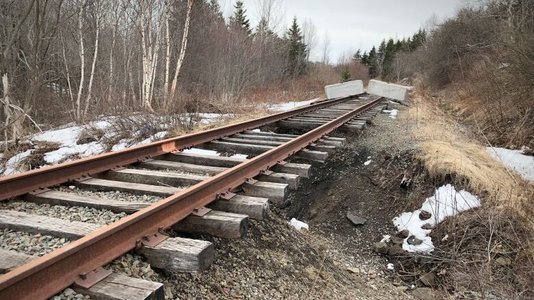 Image shows railway tracks with the gravel bed washed out underneath and concrete jersey barriers placed across the tracks.