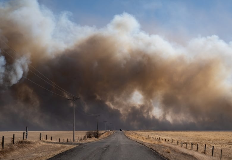 Smoke billows in the distance beyond a narrow highway.