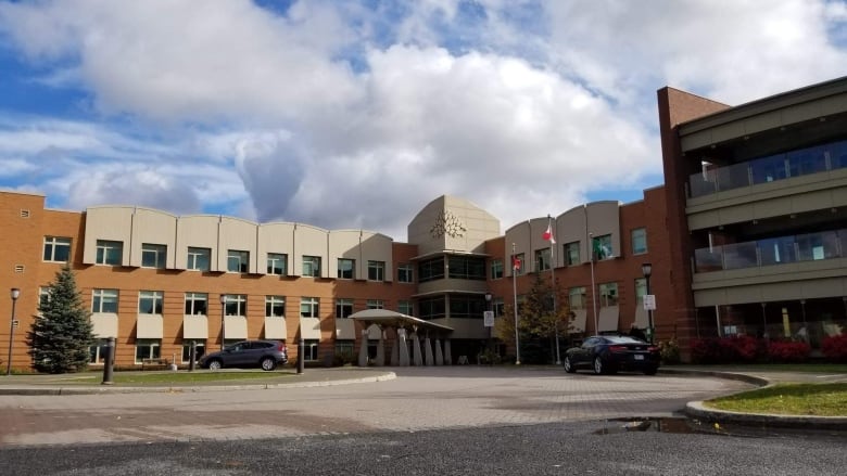 The front of a tan building with windows is seen under a blue and cloudy sky.