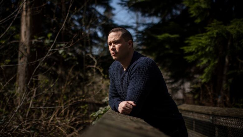 A man places his arms on a rock outside.