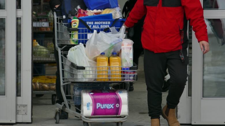 A person exiting a store with a full shopping cart.