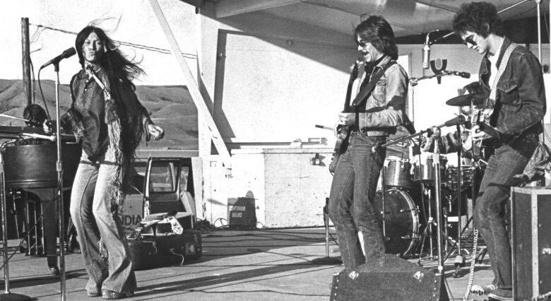 A woman sings while two guitarists play on a stage.