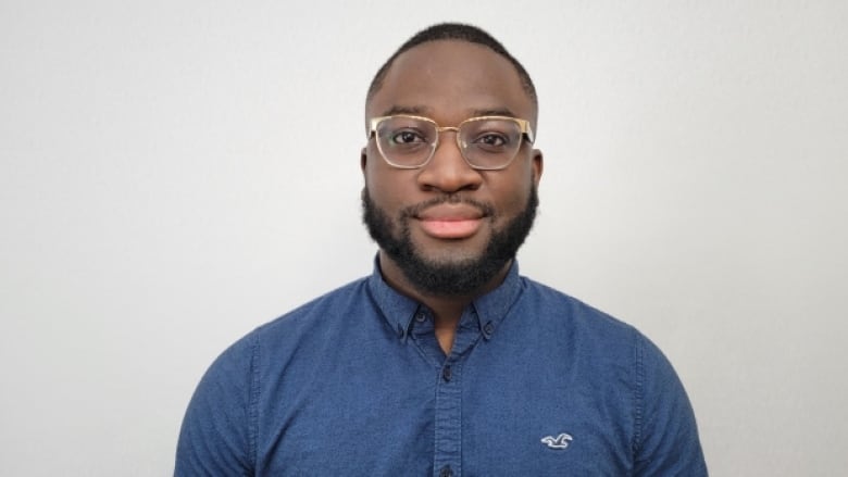 A bearded Black man with glasses wearing a blue shirt.