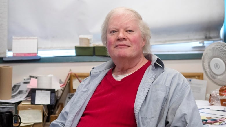 A man sits at a messy desk in an office.