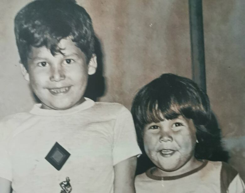 A black and white photograph shows two smiling boys standing side-by-side.