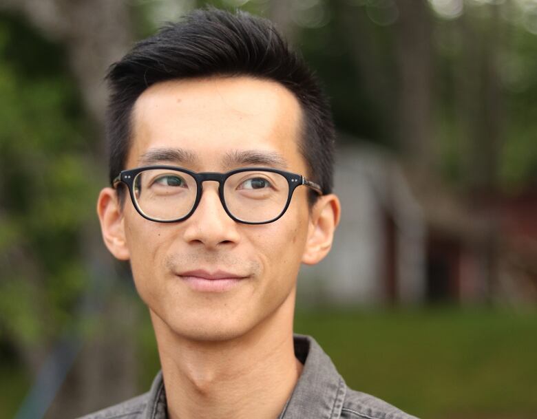 A man with short, dark hair and glasses smiles slightly, looking away from the camera.