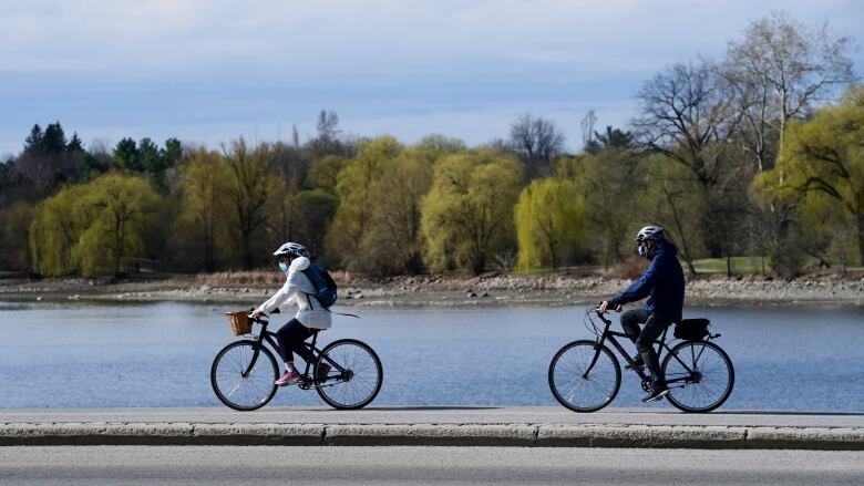 Masked cyclist ride alongside a lake.