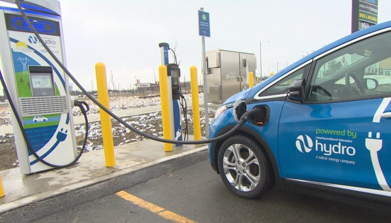 A car is parked next to an electric car charger and is plugged in to charge.