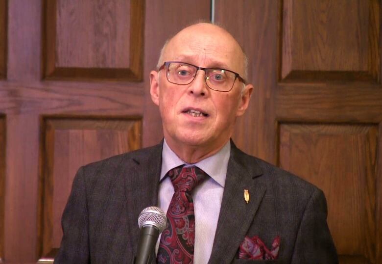 A man in glasses and a suit speaks into a microphone.