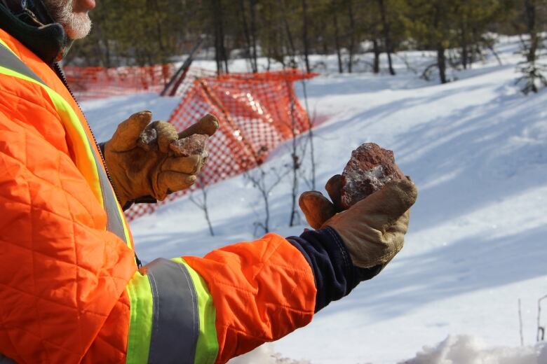 A close up of a person in a bright orange safety coat and gloves holding up a piece of rock.