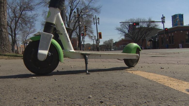 An e-scooter seen on the street with traffic lights visible in the distance. The e-scooter has no rider and is parked. 