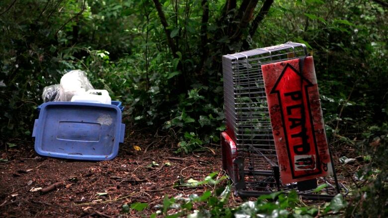 A blue tub and a shopping cart upended in green space.